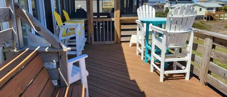 A wooden deck with outdoor seating, including chairs and a table, overlooking a residential area.