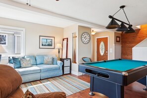 A cozy living room with a pool table, a sofa, a lamp, and a clock on the wall. - Carolina Hideaway -- Kitty Hawk Home just steps to the beach with Elevator (Kitty Hawk)
