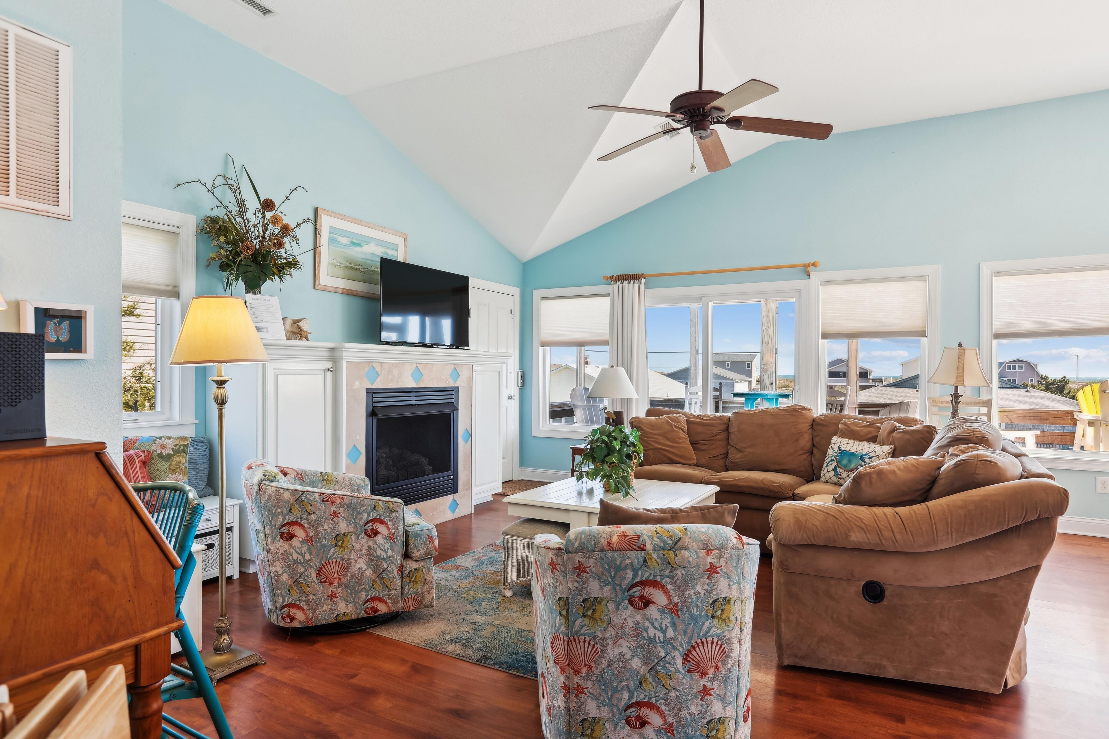 A living room with a fireplace, a ceiling fan, and a view of the ocean.