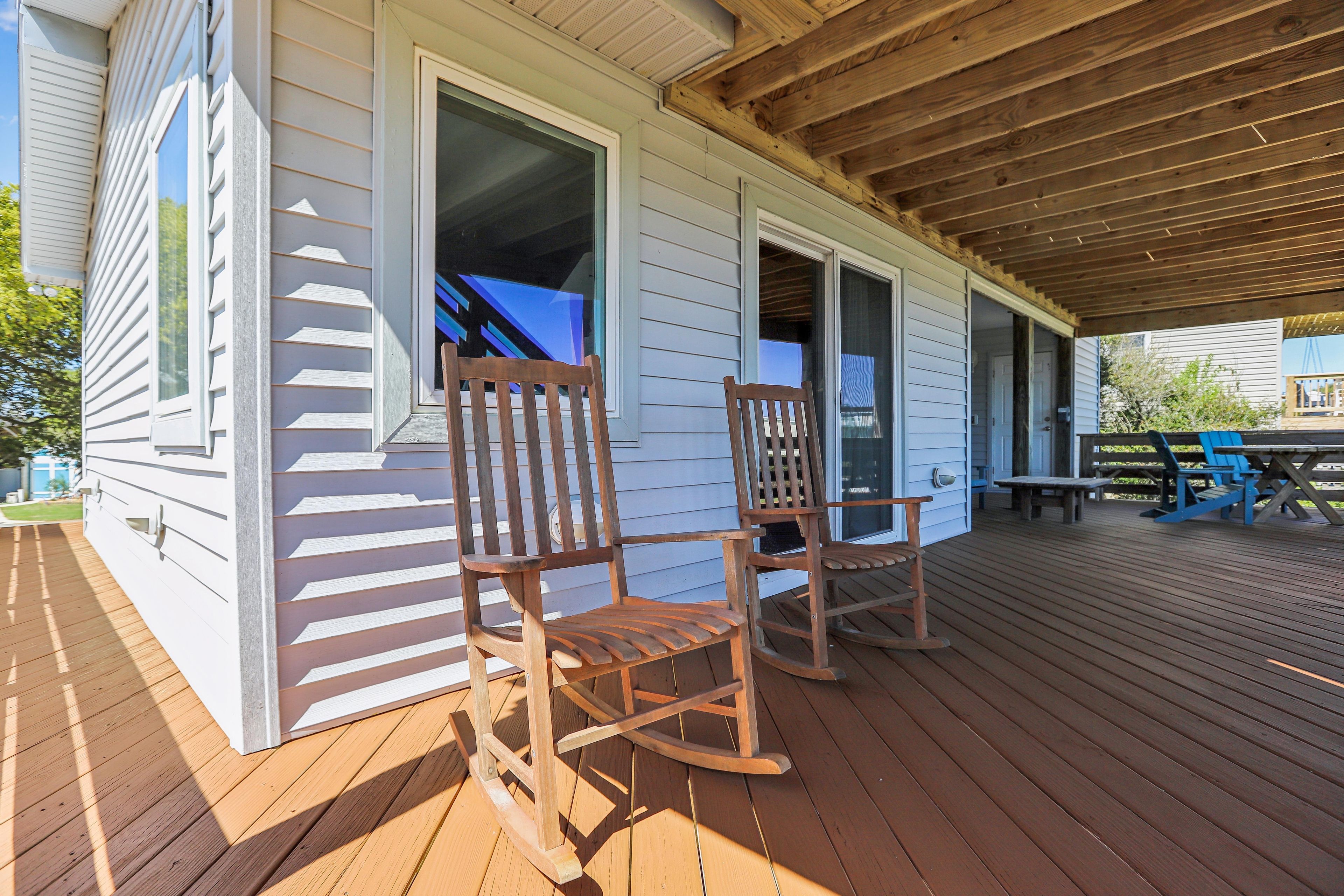 A wooden deck with two rocking chairs, a covered porch, and a view of the house.