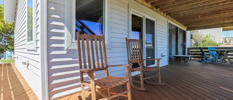 A wooden deck with two rocking chairs, a covered porch, and a view of the house.