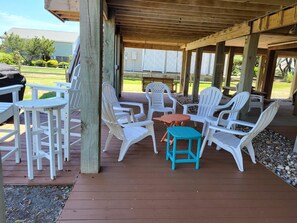 An outdoor covered patio with white plastic chairs and a small table, surrounded by wooden pillars and a wooden deck.