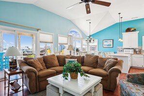 A spacious living area with a large brown sofa, a white coffee table, and a dining area with a kitchen in the background. - Carolina Hideaway -- Kitty Hawk Home just steps to the beach with Elevator (Kitty Hawk)