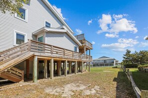 Enjoy the expansive deck with a staircase leading up to a second-floor balcony overlooking a serene lawn and walkway.