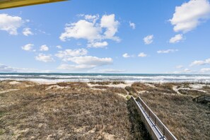 A beach with a wooden boardwalk leading to the ocean, under a clear sky.