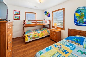 A bedroom with a bunk bed, wooden dresser, and a window with blinds. - Lovelady -- Pet Friendly Oceanfront with Hot Tub (Kill Devil Hills)