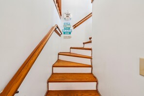 A wooden staircase with white risers and a handrail, leading to a landing with a welcome sign and a flip flop zone sign.