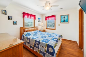 A bedroom with a bed, a desk, a ceiling fan, and windows with curtains.