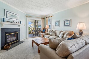 A living room with a fireplace, a sofa, a coffee table, and a view of the outside.