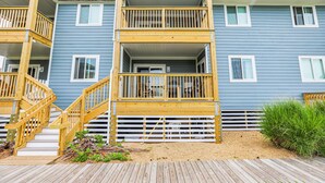 A multi-story residential building with a wooden deck and stairs leading to the entrance. - Duck Legacy -- 3BR Oceanfront Condo 2nd Floor with Ocean Views (Duck)