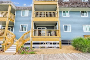 A multi-story residential building with a wooden deck and stairs leading to the entrance. - Duck Legacy -- 3BR Oceanfront Condo 2nd Floor with Ocean Views (Duck)
