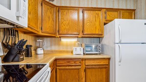 A kitchen with wooden cabinets, a microwave, a toaster, and a refrigerator. - Duck Legacy -- 3BR Oceanfront Condo 2nd Floor with Ocean Views (Duck)