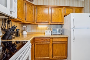 A kitchen with wooden cabinets, a microwave, a toaster, and a refrigerator. - Duck Legacy -- 3BR Oceanfront Condo 2nd Floor with Ocean Views (Duck)
