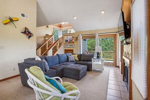 A spacious living room with a large sectional sofa, a white chair, and a small table. A staircase leads to an upper level with a balcony. - A Dream Come True -- Pet Friendly Home with Hot Tub and Community Amenities (Duck)