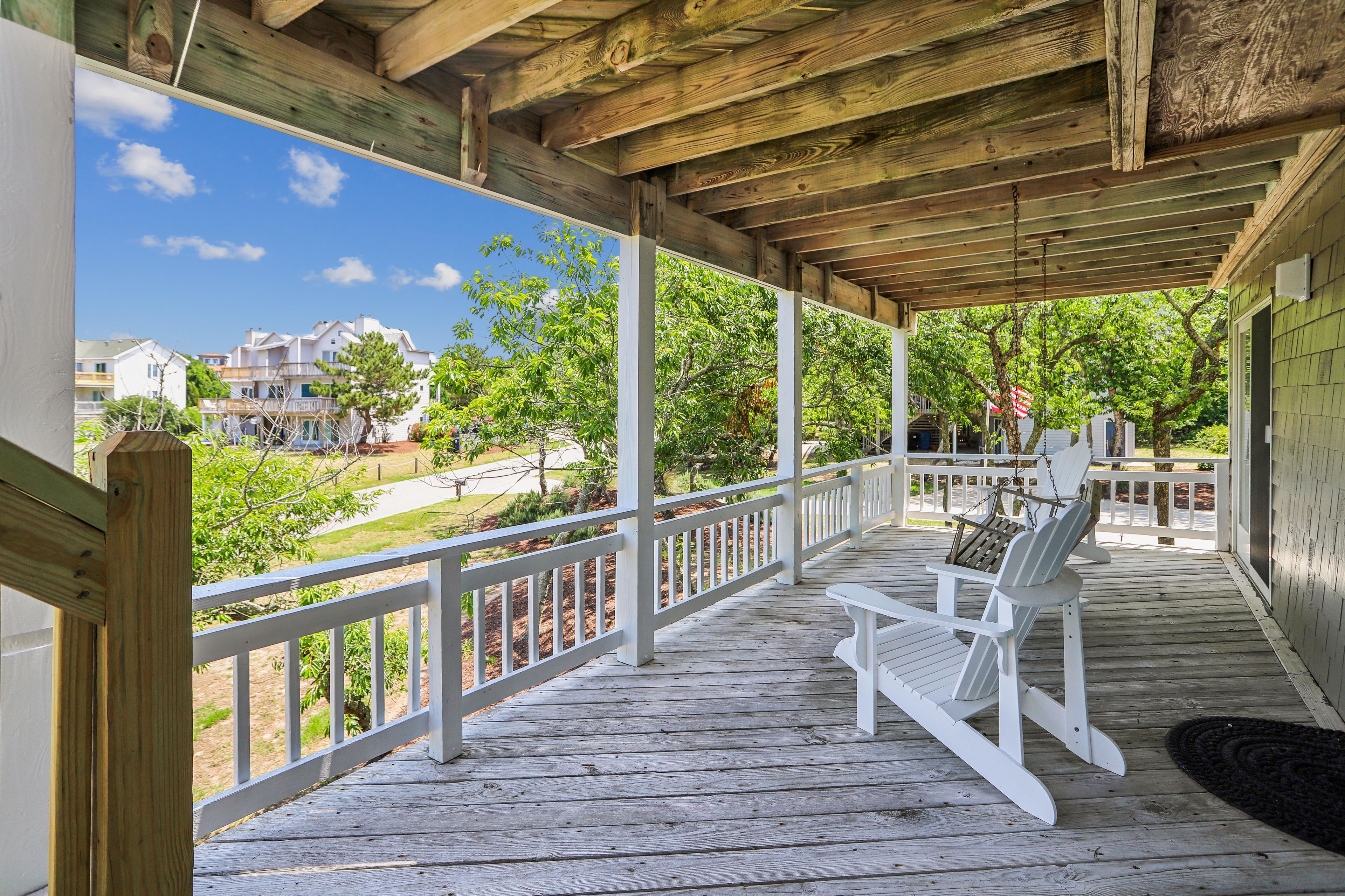 Une véranda couverte avec des balustrades blanches, un plancher en bois et des fauteuils Adirondack.