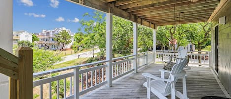 Eine überdachte Veranda mit weißen Geländern, Holzboden und Adirondack-Stühlen.