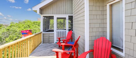 Une terrasse en bois avec des chaises rouges et une table, donnant sur un paysage verdoyant.
