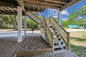 A wooden staircase with a metal railing leading to a covered area with a gravel base. - A Dream Come True -- Pet Friendly Home with Hot Tub and Community Amenities (Duck)
