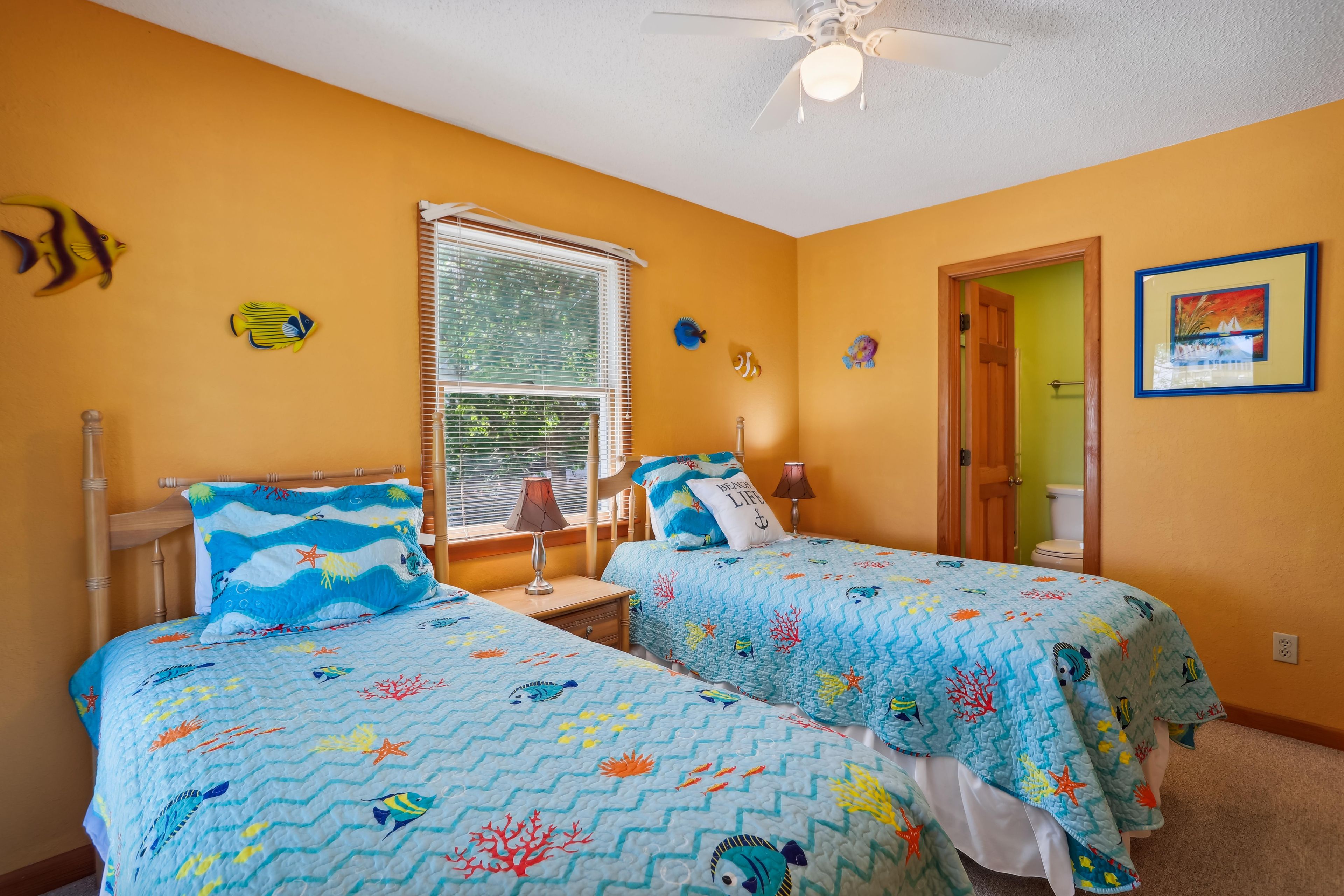 A bedroom with two beds, a window with blinds, a ceiling fan, and a painting on the wall.