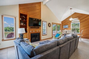 A spacious living room with a large sofa, a flat-screen TV, a fireplace, and a ceiling fan.