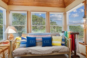 A room with a bed, a lamp, and a view of trees through large windows.