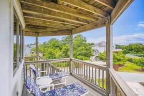 Une terrasse en bois avec un porche couvert, du mobilier d’extérieur et une vue sur un quartier résidentiel.