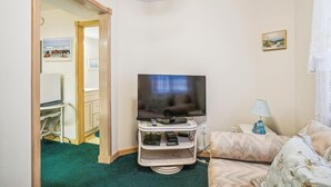 A room with a television on a stand, a sofa, a lamp, and a painting on the wall.