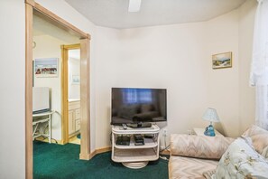 A room with a television on a stand, a sofa, a lamp, and a painting on the wall. - Crystal Sands -- Unique 5 BR in Southern Duck with Community Amenities (Duck)