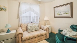 A room with a beige sofa, a green armchair, a white lamp, and a framed landscape painting.