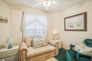 A room with a beige sofa, a green armchair, a white lamp, and a framed landscape painting. - Crystal Sands -- Unique 5 BR in Southern Duck with Community Amenities (Duck)