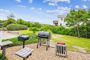A backyard with a grill, a trash can, and a bench. - Duck Views-- 4BR Oceanside Duck Home with Private Pool (Duck)