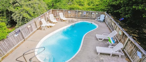A swimming pool with a wooden deck, surrounded by a wooden fence and trees.