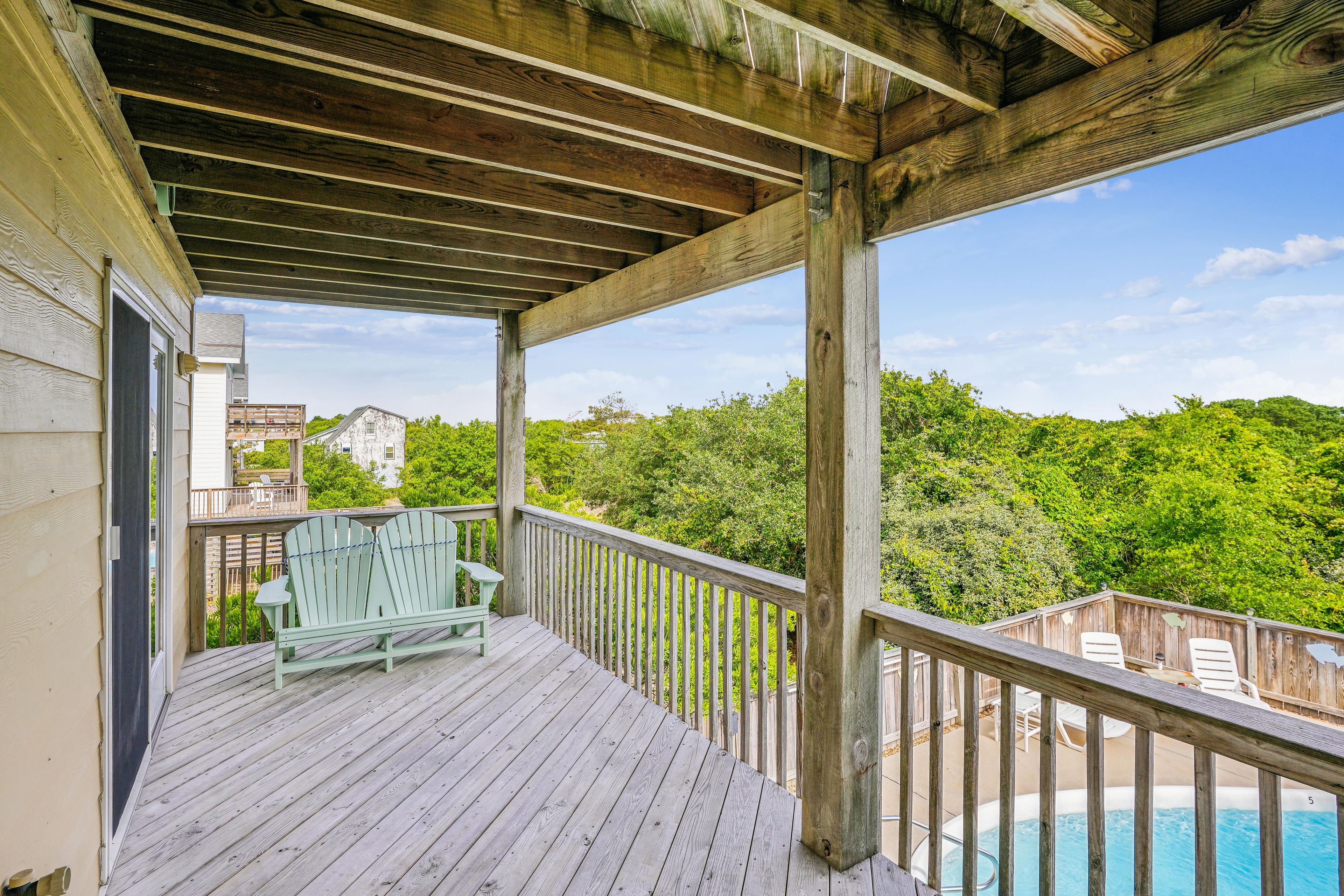 A wooden deck with a pool, a chair, and a view of a forested area.