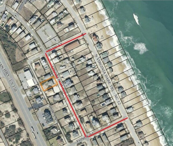Vista aérea de una zona residencial costera con manzanas de casas, una línea roja que indica una calle y una playa al fondo.