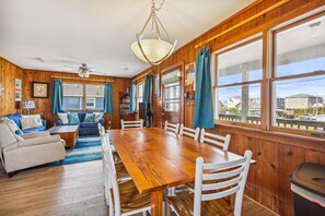 A spacious living room with a wooden dining table, white chairs, and a blue sofa.