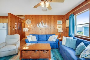 Een gezellige woonkamer met een blauwe bank, een houten plafondventilator en decoratie met nautische thema's.