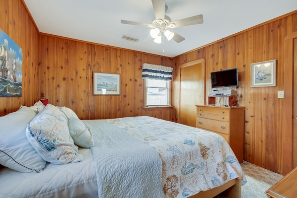 A bedroom with a bed, a dresser, a television, and wooden walls.