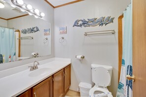 A bathroom with a white sink, a toilet, a mirror with lights, and a shower curtain.