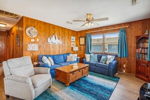 Ein gemütliches Wohnzimmer mit einem blauen Sofa, einem Holztisch und einem Deckenventilator.