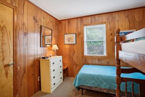 Quarto com paredes de madeira, uma cama de solteiro, cômoda e duas fotos emolduradas.
