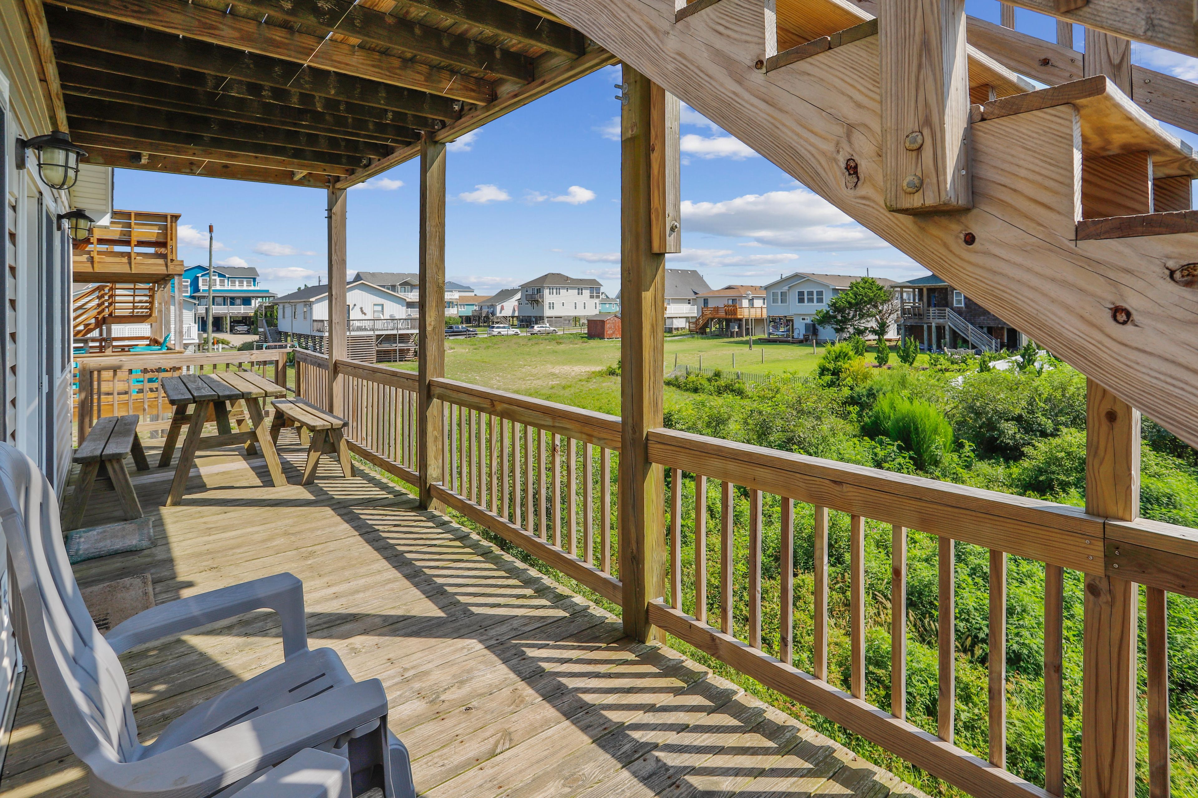 A wooden deck with picnic tables and a railing overlooking a residential area.