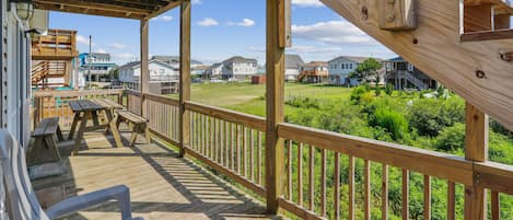 A wooden deck with picnic tables and a railing overlooking a residential area.