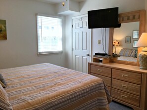 A bedroom with a bed, a dresser, a television, and a window with blinds. - School Bored --Affordable Cottage just 2 blocks to the ocean (Kill Devil Hills)