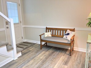 Un banco de madera con dos almohadones, una puerta con ventanal y una escalera con descansillo alfombrado.