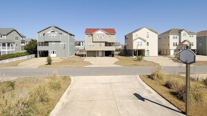 Una calle residencial con casas, cielo despejado y un aro de baloncesto.
