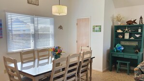 Un comedor con mesa y sillas de madera, un jarrón de flores y un estante verde con adornos.