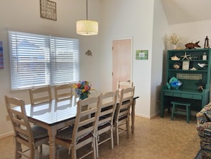 A dining area with a wooden table and chairs, a vase of flowers, and a green shelf with decorative items.