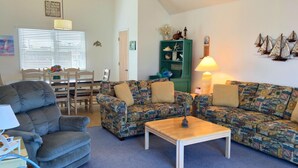 Ein Wohnzimmer mit einer Couch, einem Sessel, einem Couchtisch und einem Essbereich mit Tisch und Stühlen.