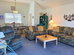 A living room with a sofa, armchair, coffee table, and a dining area with a table and chairs. - School Bored --Affordable Cottage just 2 blocks to the ocean (Kill Devil Hills)