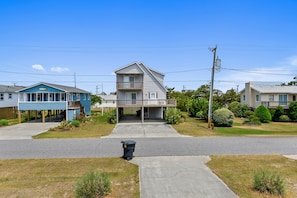 A two-story residential building with a garage, a front yard with grass and shrubs, and a clear sky.